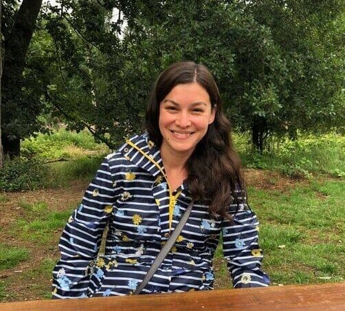 Portrait picture of Marina Hall, long dark hair, smiling in front of trees